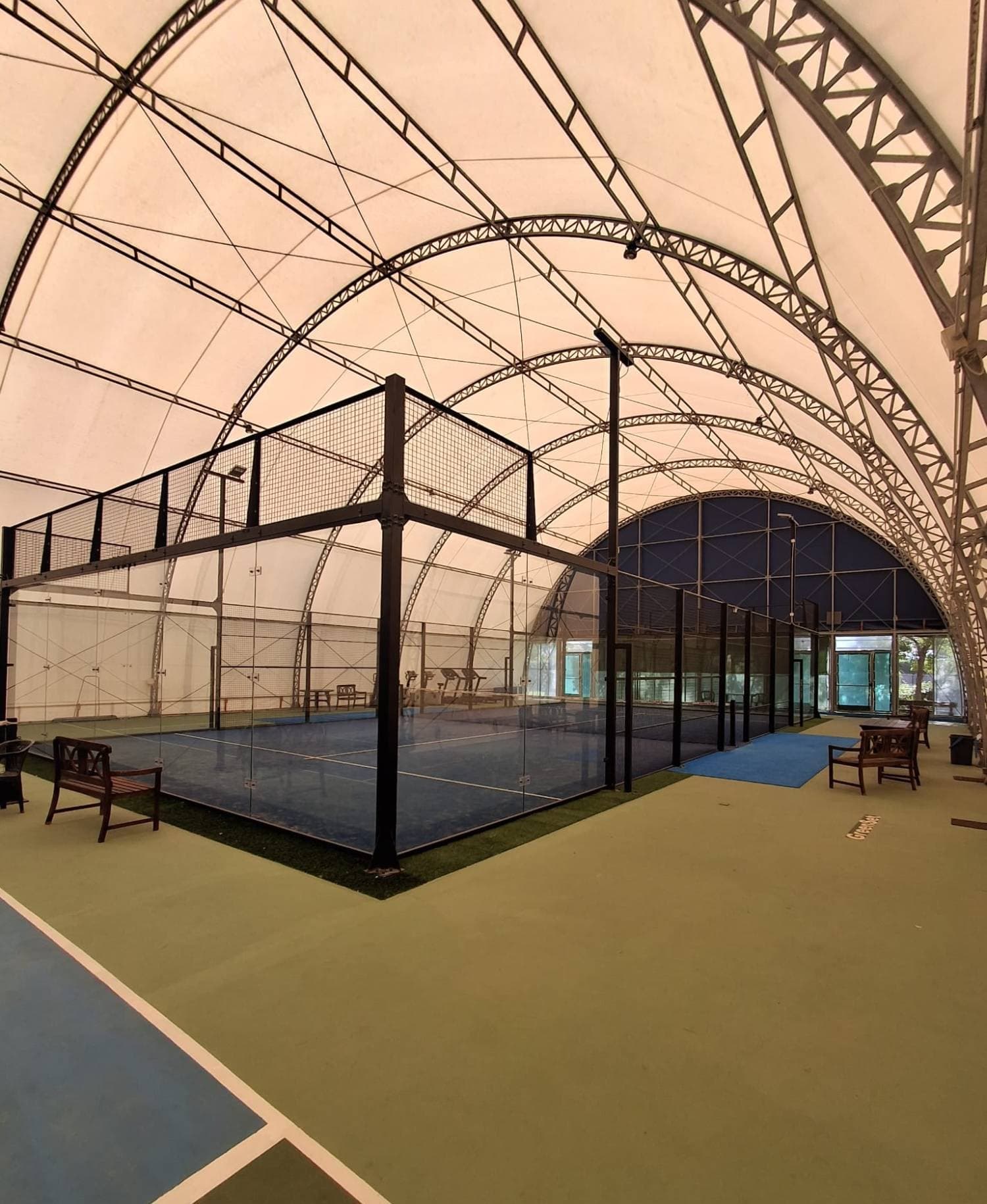 Campo da padel con pareti in vetro sotto la tensostruttura, con panchine in legno